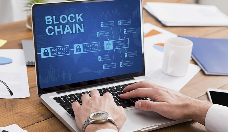 Homem digitando no computador que mostra a tela de uma cadeia blockchain.