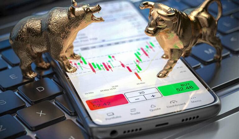 Urso e touro de ouro em miniatura em cima de um celular com gráficos de investimento.